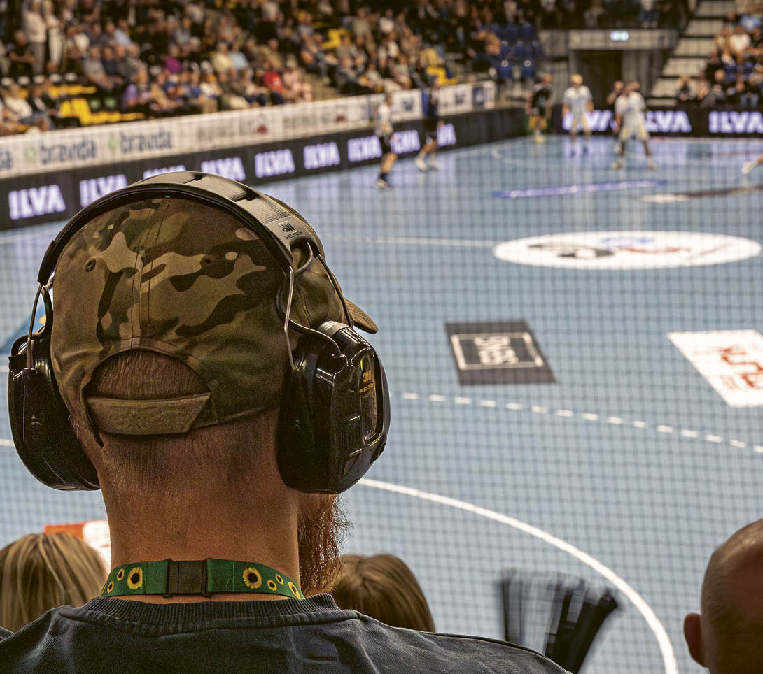 A man wearing a camouflage hat and headphones is watching a basketball game. Description generated by AI
