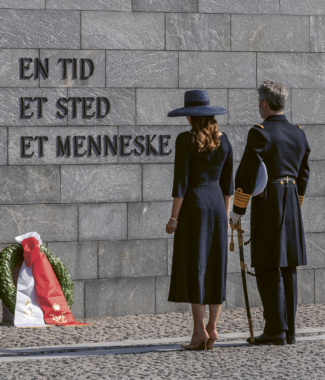A man and woman standing in front of a wall with a hat on the woman. Description generated by AI
