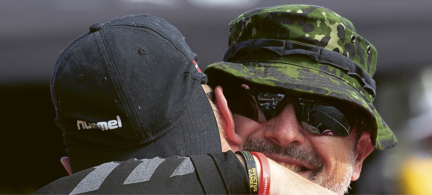 Two men wearing camouflage hats and sunglasses hugging each other. Description generated by AI