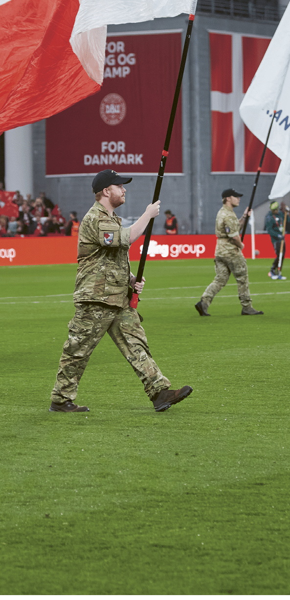 A group of men in camouflage uniforms are holding flags on a soccer field. Description generated by AI