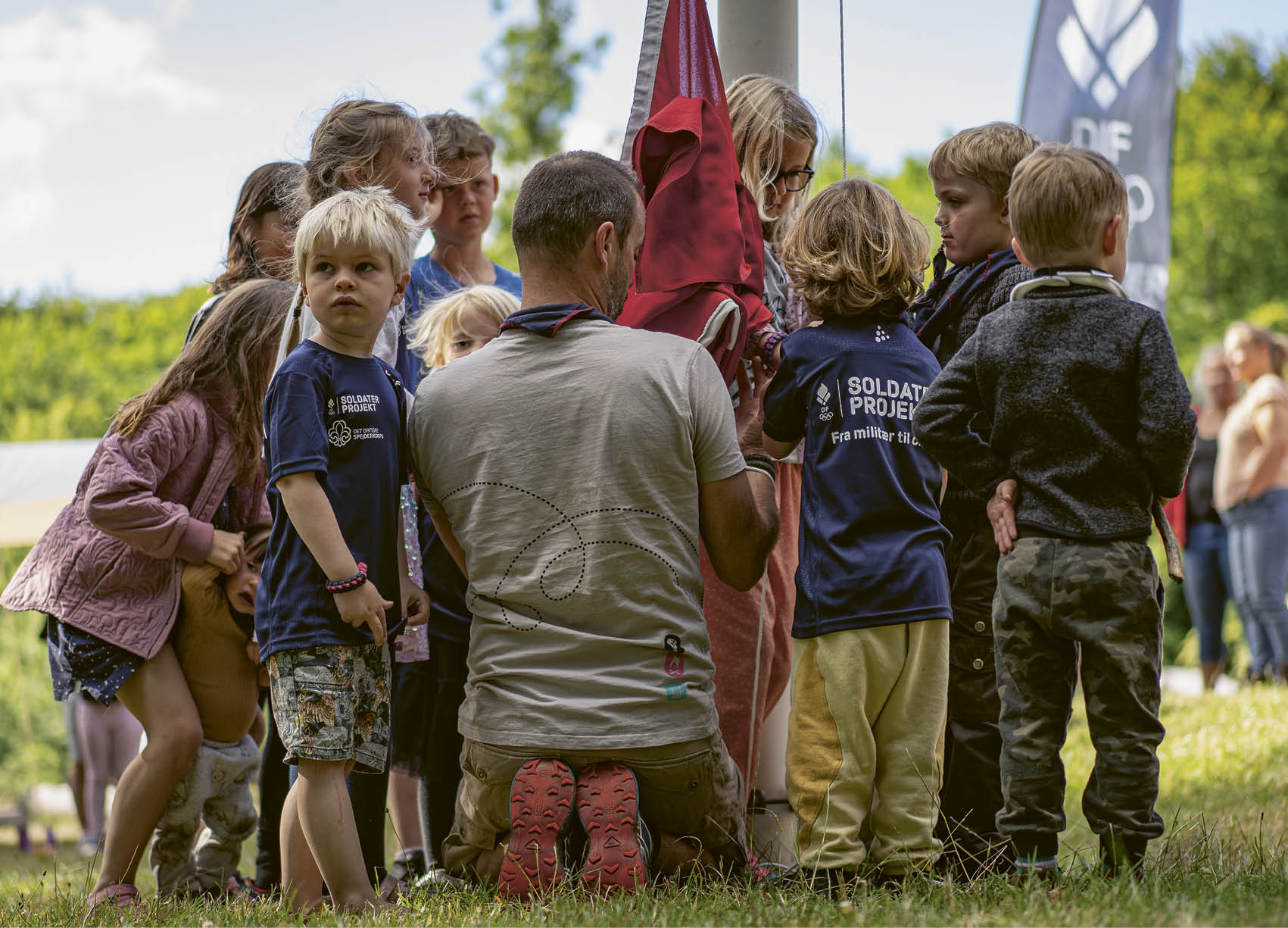 A group of children and adults are gathered around a flag. Description generated by AI