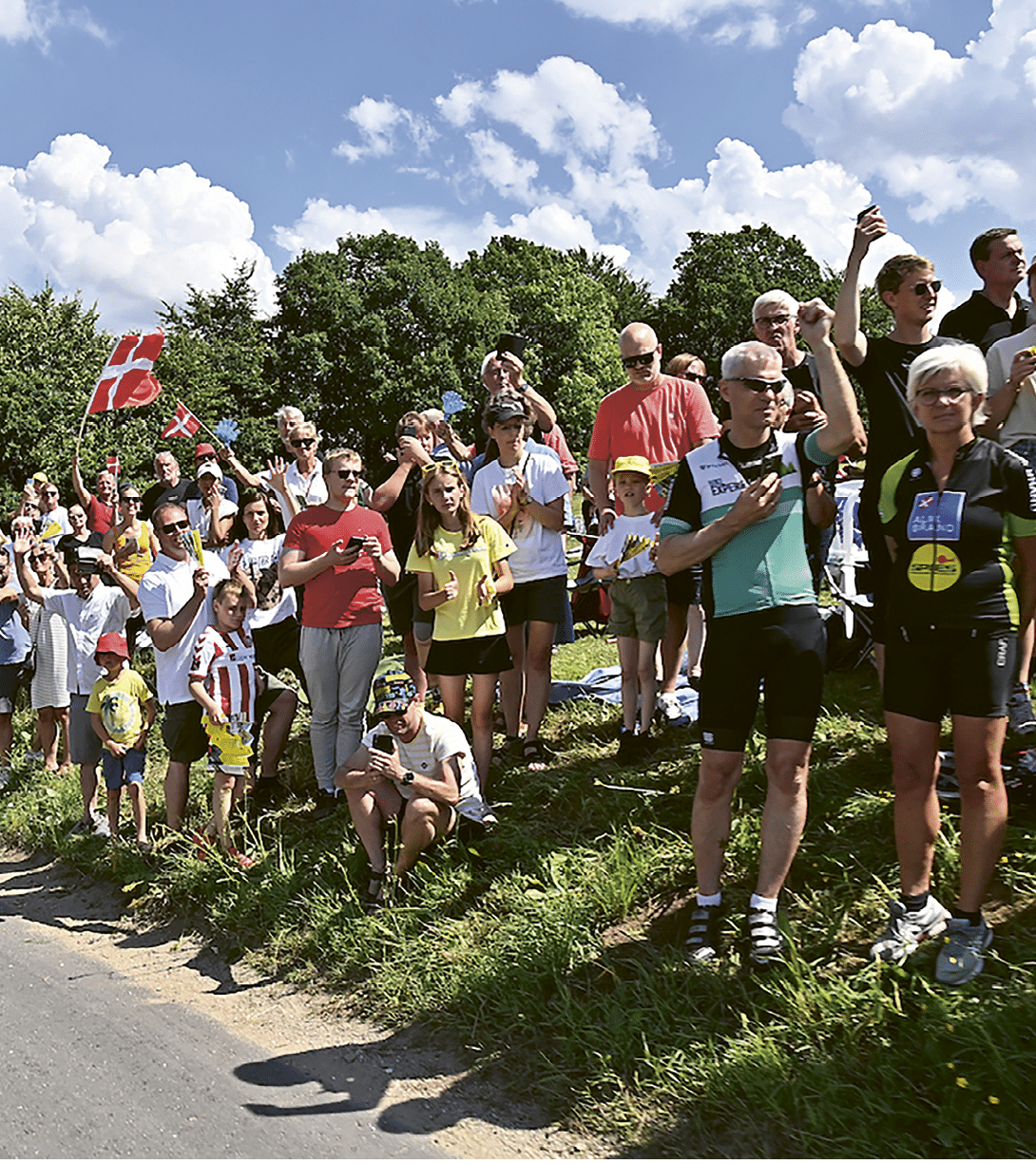 A crowd of people are standing on a grassy hill, watching a race. Description generated by AI