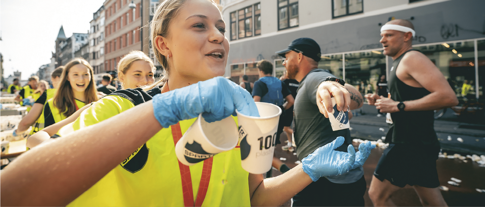 A woman wearing a yellow shirt and blue gloves holds a cup. Description generated by AI